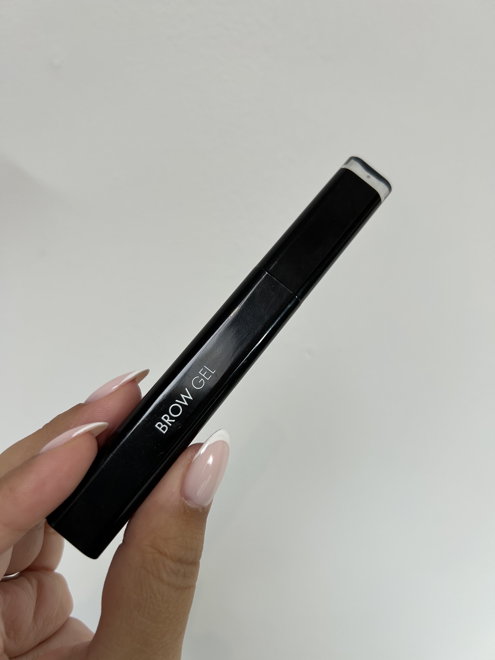 Hand met lichtroze nagels die een zwarte tube Brow Gel vasthoudt